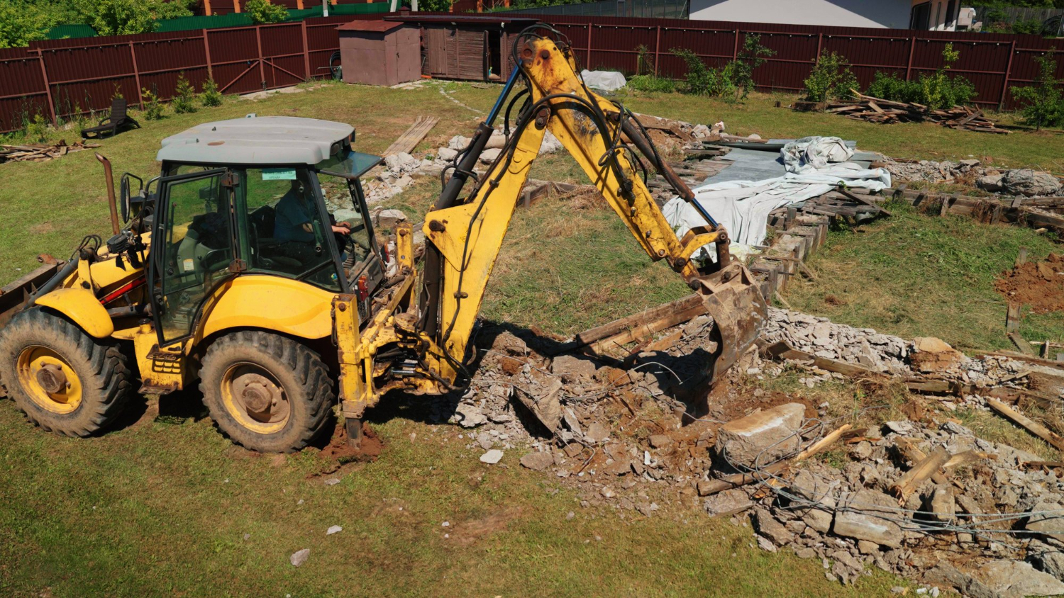 Residential excavation job with excavator removing soil, concrete, and debris from a backyard construction site.