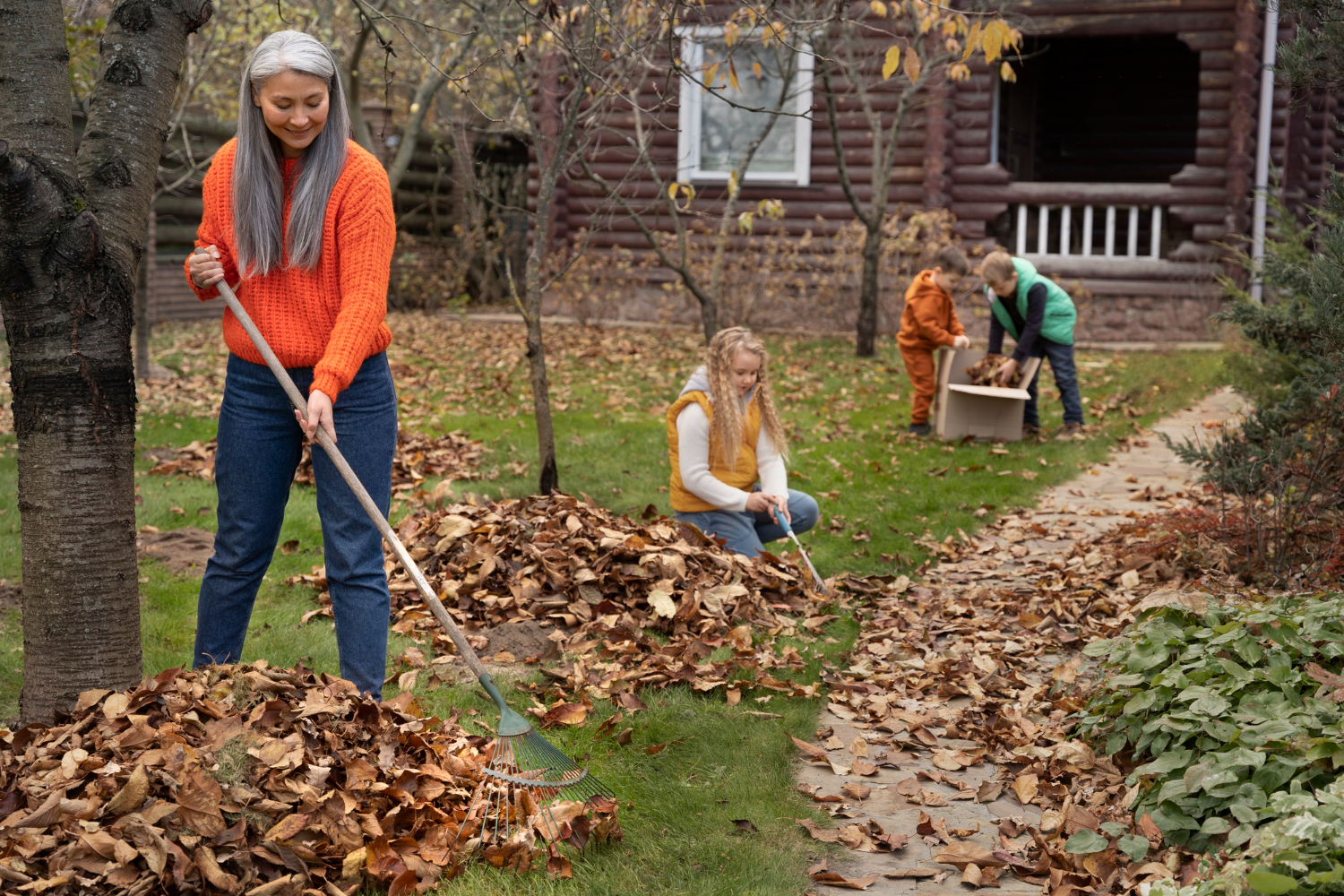 Family raking and collecting fallen leaves during fall yard cleanup in a residential lawn.
