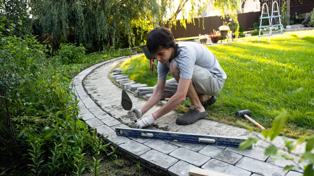 Paver walkway installation in Richmond VA with landscaper laying stone blocks along a residential garden path landscape.